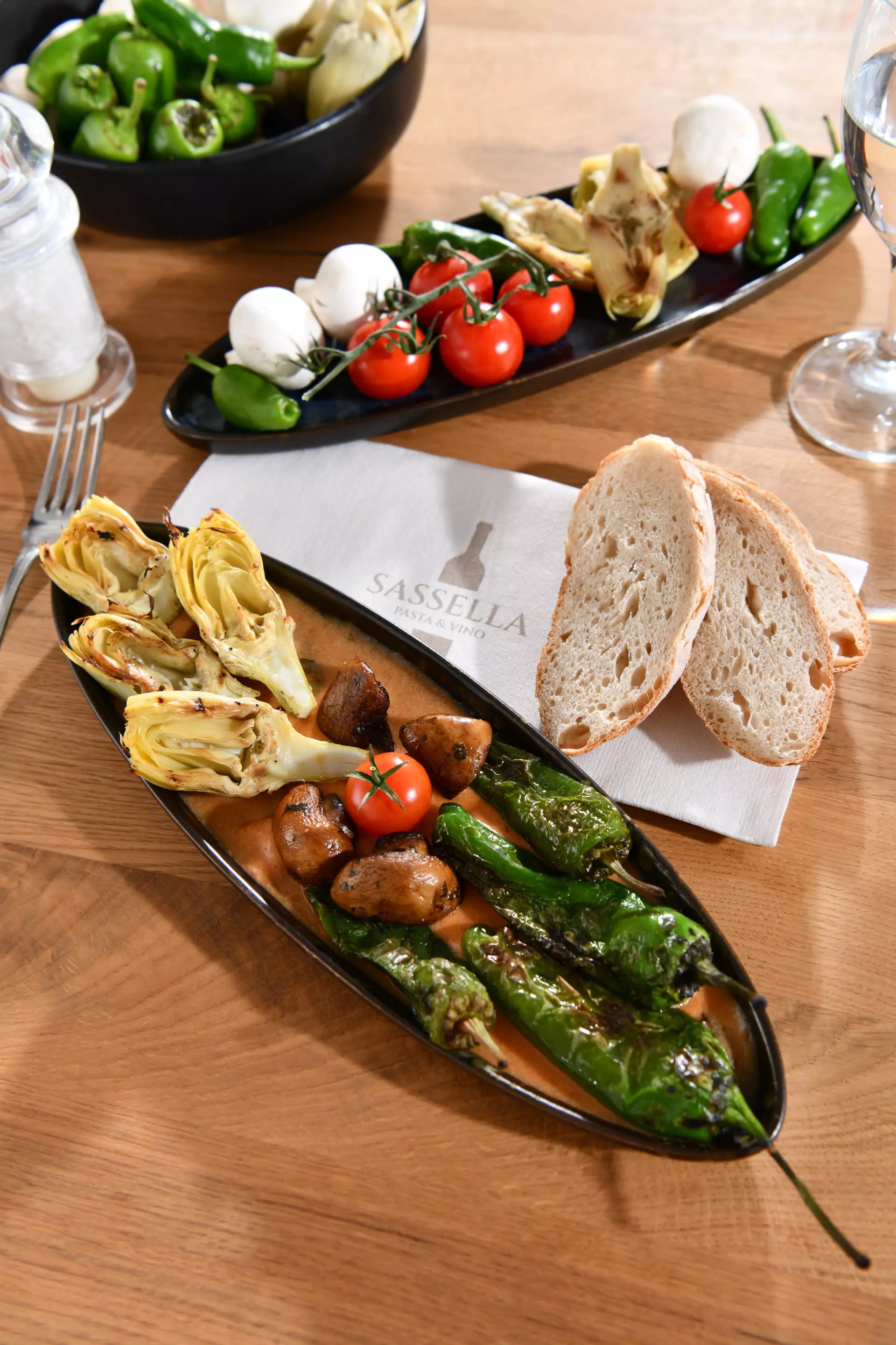 Antipasti-Platte mit gegrillten Artischocken, Pimientos de Padrón, Kirschtomaten, Mozzarella-Bällchen und Brot.