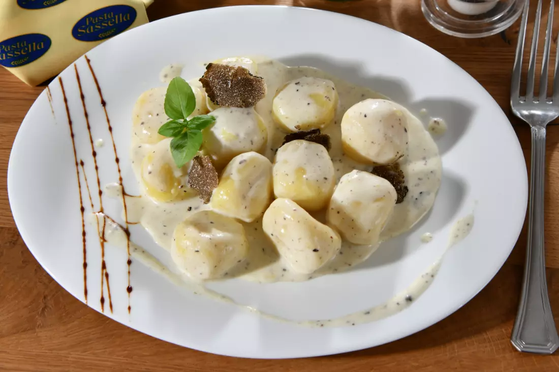 Gnocchi in cremiger Soße, garniert mit Trüffelscheiben und einem Basilikumblatt, auf einem weißen Teller.
